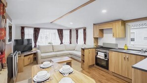 Un espacio habitable compacto con sofá, mesa de comedor para cuatro personas, kitchenette y televisor.
