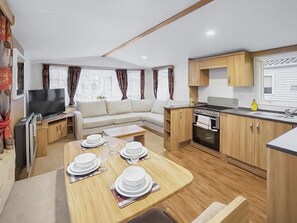 A compact living space with a sofa, dining table set for four, a kitchenette, and a television. - Gold Series - 2 - UK51707 (Sandown)