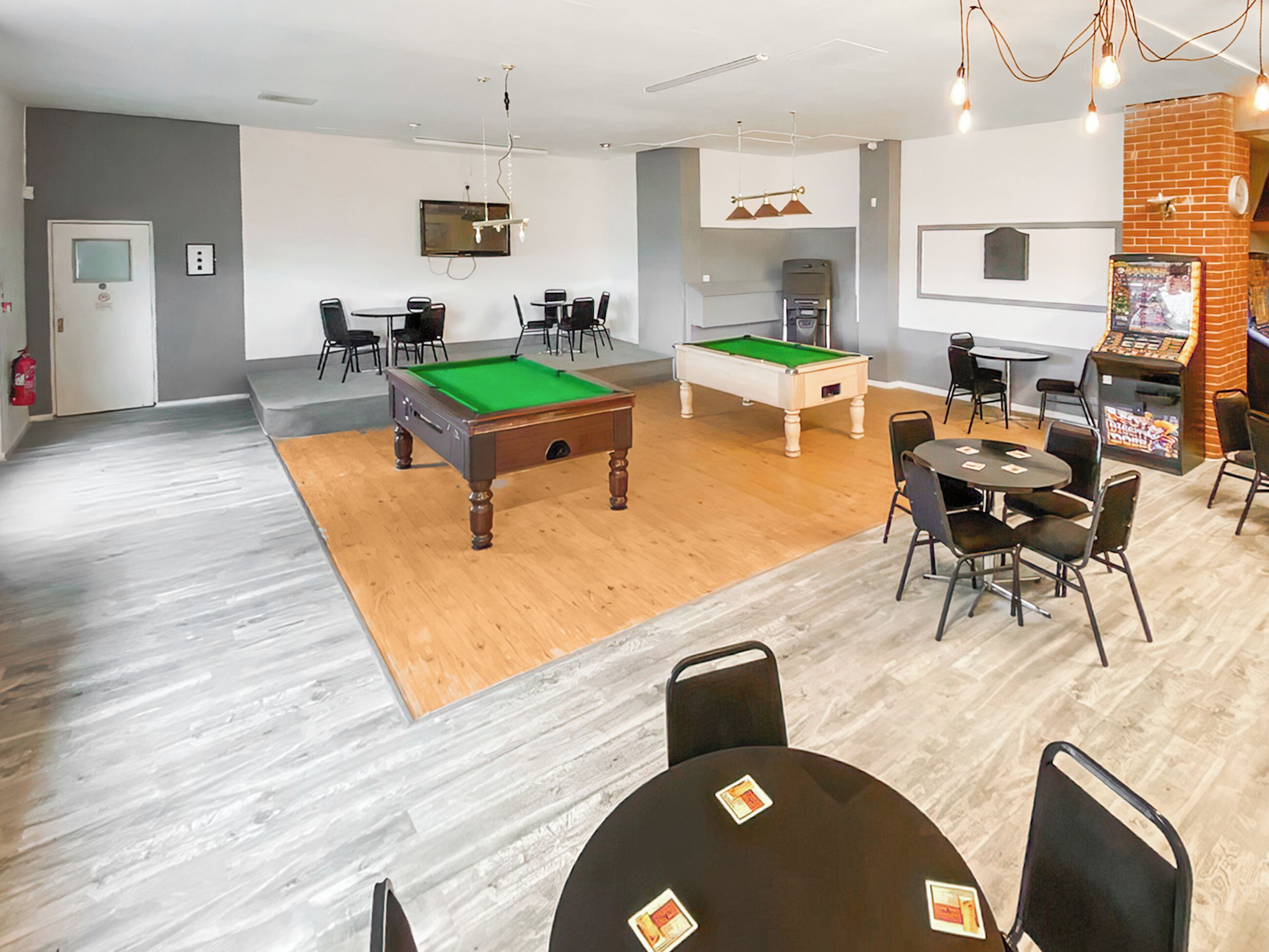 A room with a pool table, chairs, a television, and a snack bar.