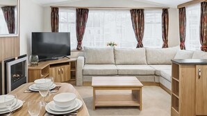 Interior moderno de una caravana con sofá, televisor, mesa de comedor y zona de cocina.