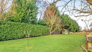 Ein gepflegter Garten mit verschiedenen Bäumen, einer ordentlich geschnittenen Hecke und einer kleinen Holzkonstruktion.