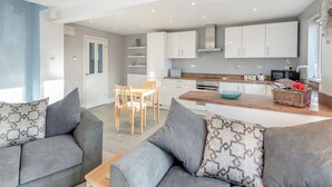 Eine moderne Küche mit weißen Schränken, ein Essbereich mit Tisch und Stühlen sowie ein Wohnbereich mit grauen Sofas.