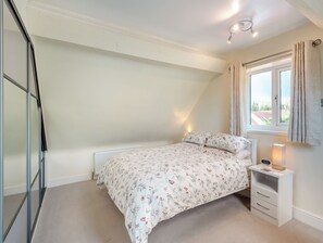 A bedroom with a bed, a bedside table with a lamp, a window with curtains, and a radiator. - 1 bedroom accommodation in Castle Bytham, near Grantham (Castle Bytham, near Grantham)