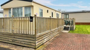 Ein Mobilheim mit Holzterrasse, einem Ziegelweg und einem kleinen Rasenstück.