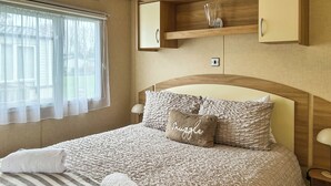 Ein ordentlich bezogenes Bett mit einem gestreiften Handtuch, einem Kopfkissen mit dem Aufdruck 'Snuggle' und einem hölzernen Kopfteil.