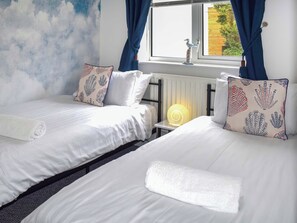 A hotel room with two beds, a radiator, a window with curtains, and a wall with a cloud pattern. - 2 bedroom accommodation in Woolacombe (Woolacombe)