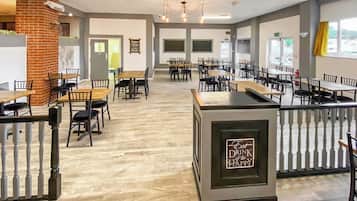 A spacious indoor dining area with multiple tables and chairs, a central counter with a sign, and a brick column.
