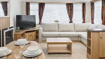 A modern RV interior with a sofa, TV, dining table, and kitchen area.