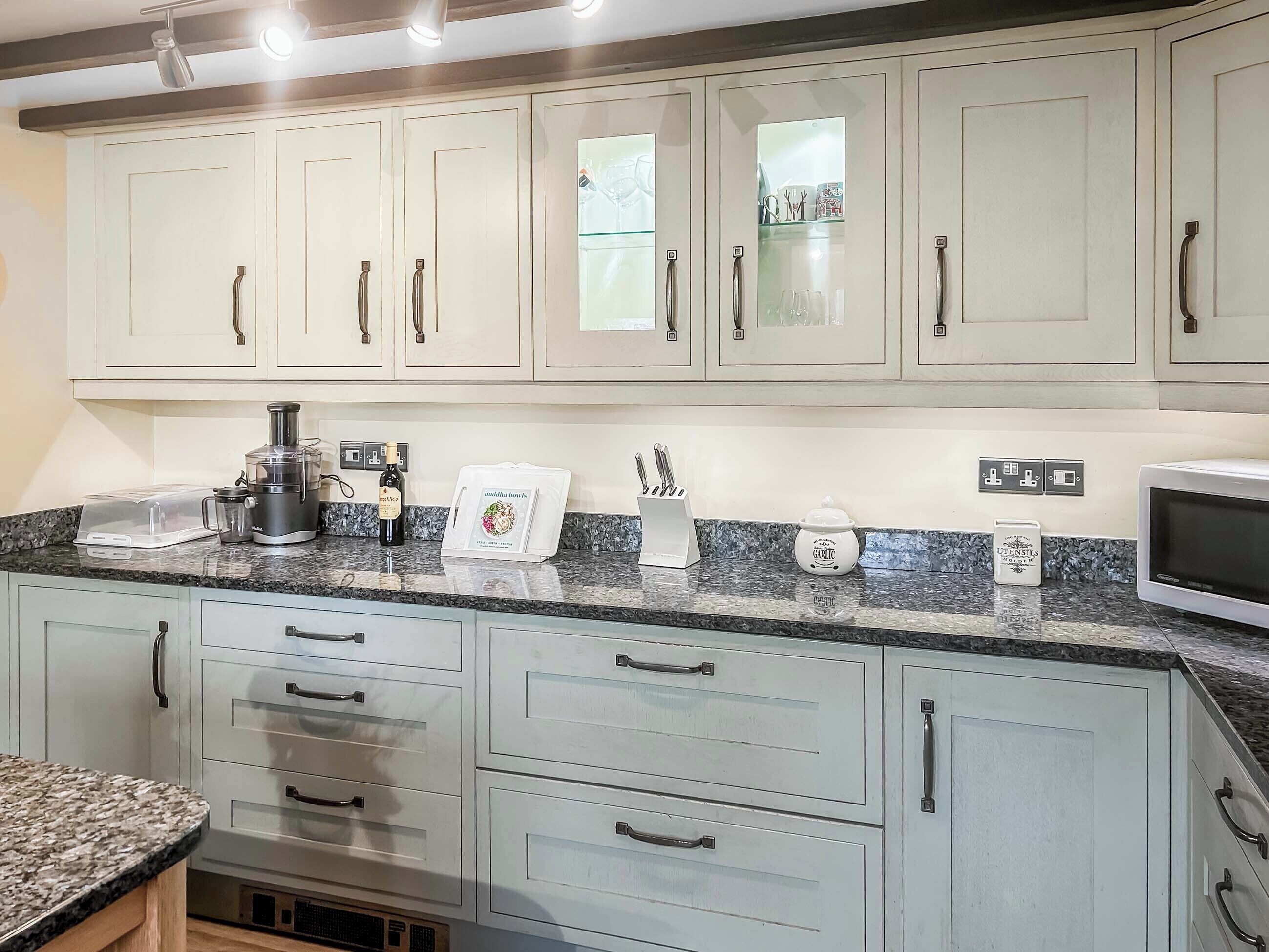 A kitchen with light-colored cabinets, a granite countertop, a coffee maker, a microwave, and a set of knives.