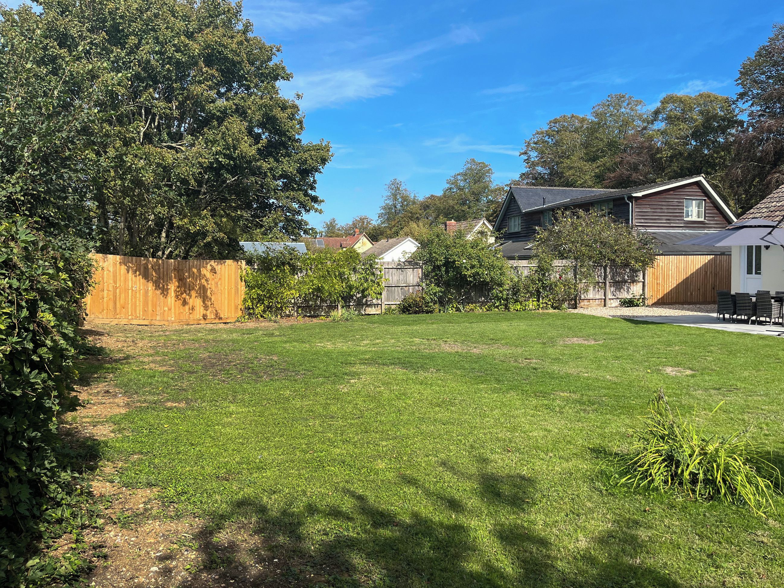 A residential backyard with a lawn, a wooden fence, and a house with a sloped roof.