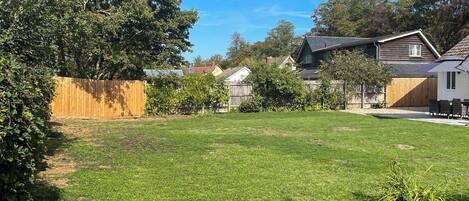 A residential backyard with a lawn, a wooden fence, and a house with a sloped roof.