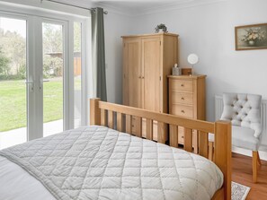 A bedroom with a bed, a wooden wardrobe, a chair, and a view of the outdoors. - 4 bedroom accommodation in Hessett, near Bury St Edmunds (Hessett, near Bury St Edmunds)