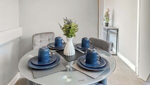 A round glass table with blue plates and matching cups, surrounded by grey upholstered chairs.