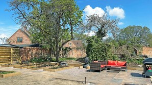 A garden with raised beds, a Buddha statue, outdoor furniture, and a brick house in the background.