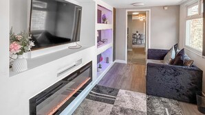 A modern living room with a flat-screen TV, a fireplace, a sofa, and a hallway leading to a dining area.