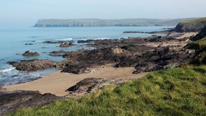 A coastal landscape with rocky terrain, a sandy beach, and a view of the sea and distant hills. - 6 bedroom accommodation in Trebetherick, near Wadebridge (Trebetherick, near Wadebridge)