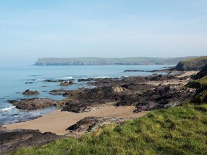 A coastal landscape with rocky terrain, a sandy beach, and a view of the sea and distant hills. - 6 bedroom accommodation in Trebetherick, near Wadebridge (Trebetherick, near Wadebridge)
