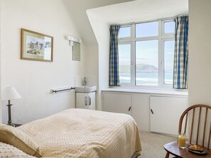 Een slaapkamer met een bed, een nachtkastje met lamp, een raam met gordijnen, een wastafel en een spiegel.