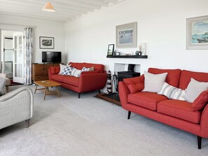 A living room with two red sofas, a wooden coffee table, a television, a fireplace, and framed artwork on the walls. - 6 bedroom accommodation in Trebetherick, near Wadebridge (Trebetherick, near Wadebridge)