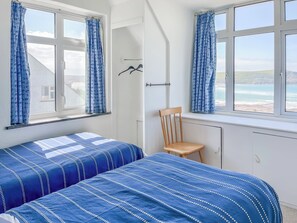 A bedroom with two beds, a chair, and a view of the sea. - 6 bedroom accommodation in Trebetherick, near Wadebridge (Trebetherick, near Wadebridge)