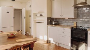 A kitchen with white cabinets, a wooden dining table, chairs, a stove, and a tiled backsplash. - 6 bedroom accommodation in Trebetherick, near Wadebridge (Trebetherick, near Wadebridge)