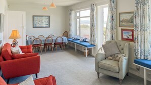 A room with a dining table, chairs, a sofa, a chair, a lamp, and a view through the window. - 6 bedroom accommodation in Trebetherick, near Wadebridge (Trebetherick, near Wadebridge)