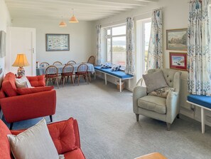 A room with a dining table, chairs, a sofa, a chair, a lamp, and a view through the window. - 6 bedroom accommodation in Trebetherick, near Wadebridge (Trebetherick, near Wadebridge)