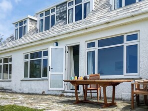 A white building with multiple windows, a wooden table with chairs, and a door open to the outside. - 6 bedroom accommodation in Trebetherick, near Wadebridge (Trebetherick, near Wadebridge)