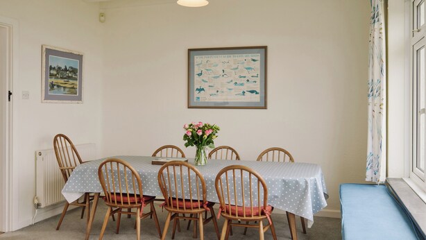 A dining area with a table, chairs, a vase of flowers, and a framed bird guide on the wall. - 6 bedroom accommodation in Trebetherick, near Wadebridge (Trebetherick, near Wadebridge)