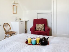 A neatly arranged room with a bed, a chair, a small cabinet, and a door. - 6 bedroom accommodation in Trebetherick, near Wadebridge (Trebetherick, near Wadebridge)