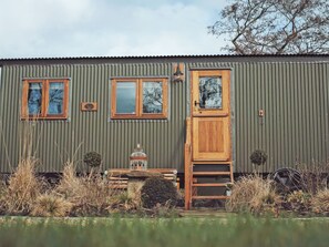 A corrugated metal building with two windows, a wooden door, and a small porch with a bench. - 1 bedroom accommodation in Mitton (Mitton)