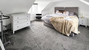 Ein modernes Schlafzimmer mit Schlafgalerie, einem Bett mit einer flauschigen Decke, einem Nachttisch mit Lampe und einer weißen Kommode.