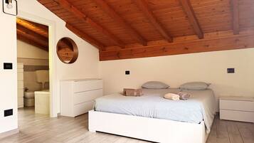 Un dormitorio con techo de madera, una cama con almohadas, una mesita de noche y un armario blanco.