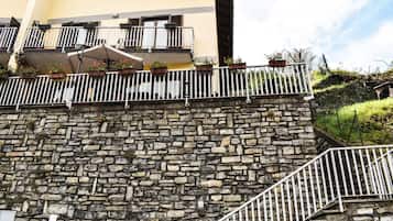 Un muro de piedra con barandilla metálica, un edificio amarillo con balcones y una escalera.
