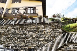 A stone wall with a metal railing, a yellow building with balconies, and a staircase. - Casa Adri (Molina)