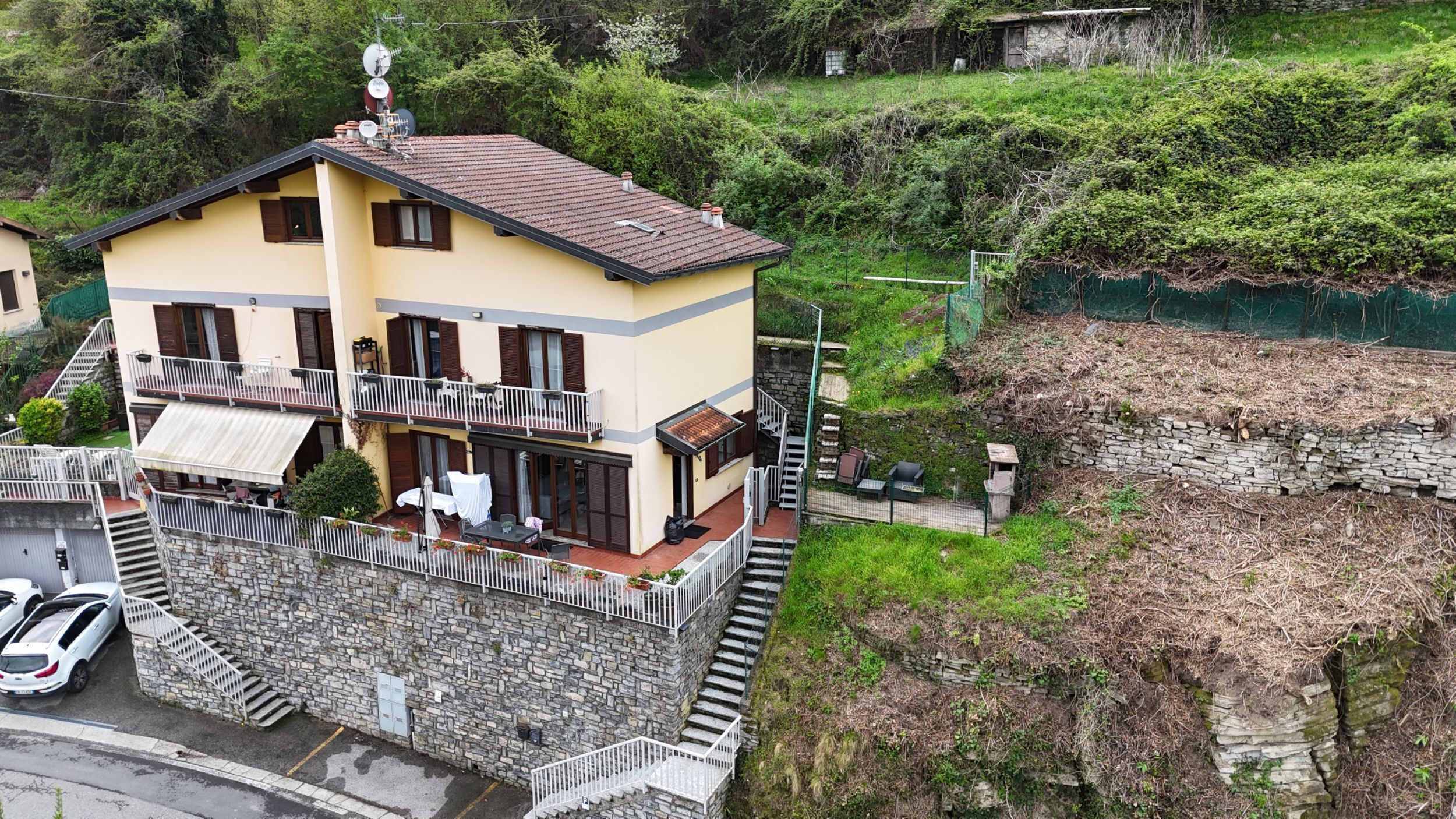 A two-story building with balconies, a stone wall, and a parking area.