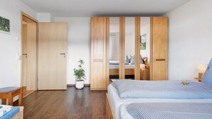 Ein modernes Schlafzimmer mit einem Holzschrank, einem Bett mit karierter Bettwäsche, einem kleinen Schreibtisch und einem Blumentopf.