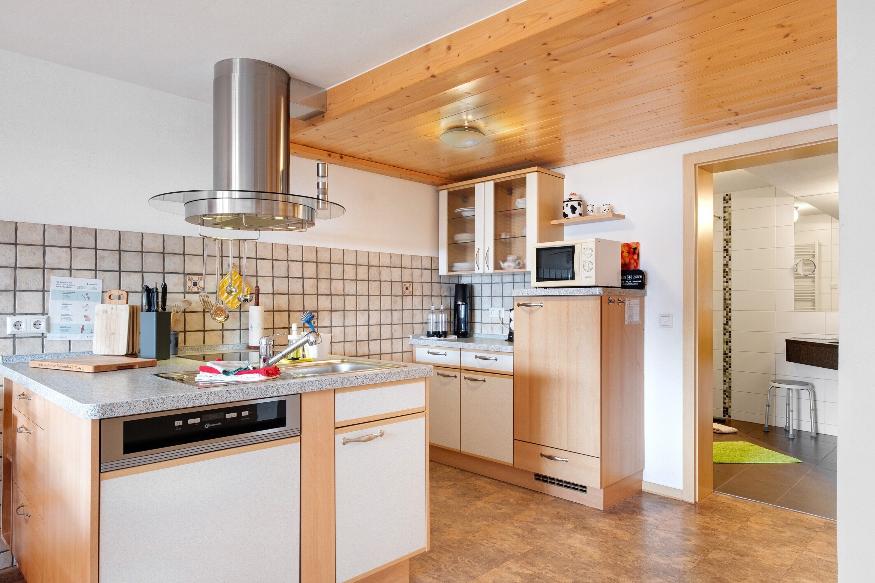 Une cuisine moderne avec des meubles en bois, un lave-vaisselle, un four à micro-ondes et une hotte aspirante en acier inoxydable.