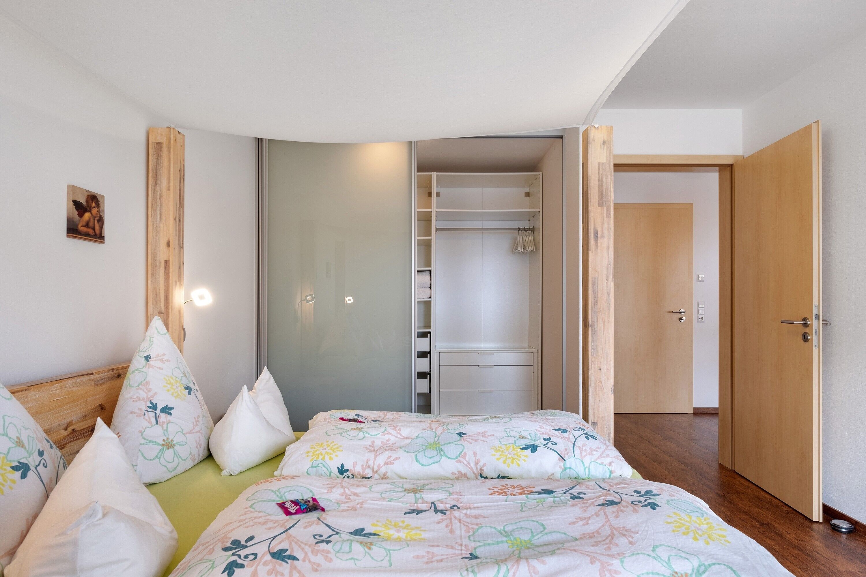 Un dormitorio con cama, almohadas, un armario y una puerta que da a otra habitación.