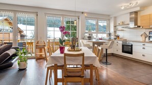 A spacious kitchen with wooden cabinets, a dining area with a table and chairs, and large windows offering a view of the outdoors.