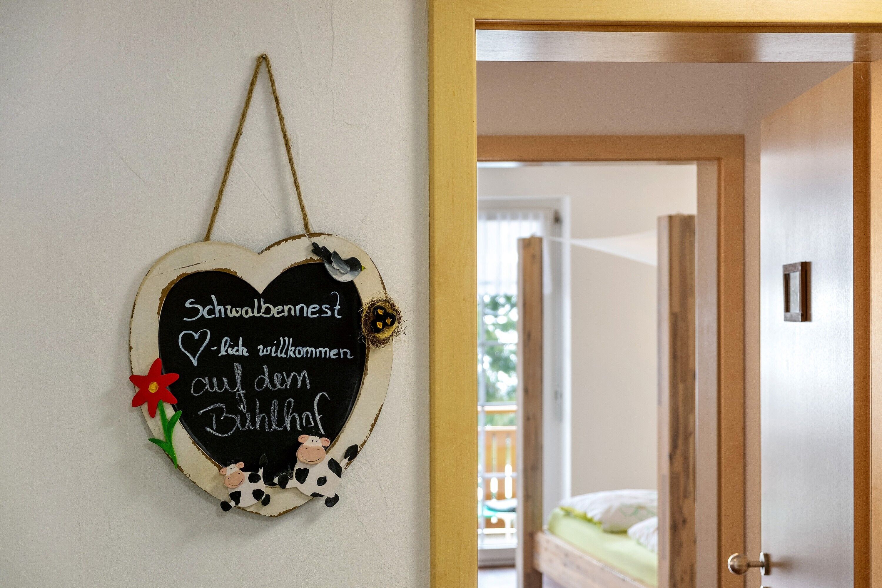 A heart-shaped sign with text in a room with a wooden door and a bed in the background.