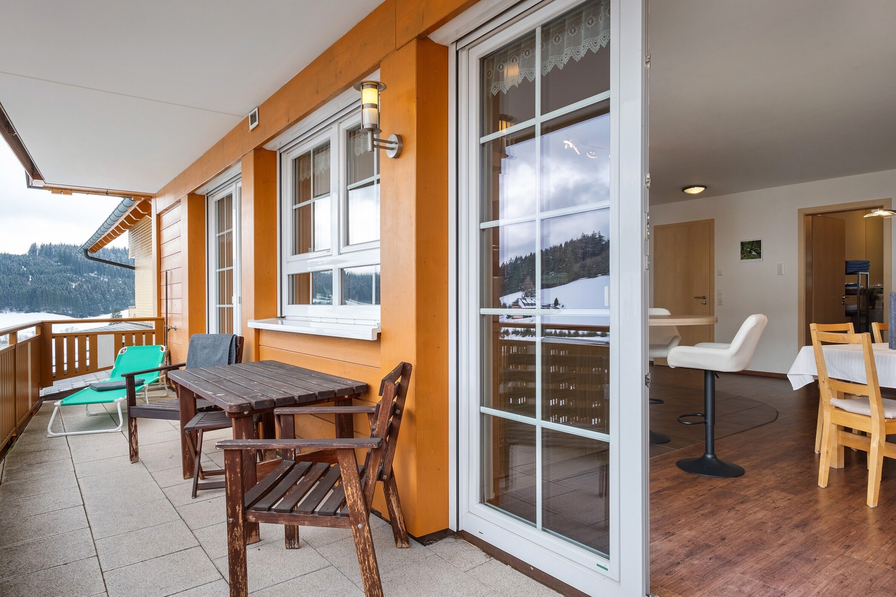 Un balcon doté de meubles en bois, de grandes fenêtres et offrant une vue sur un paysage enneigé.