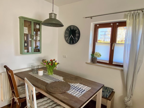 Un comedor con una mesa de madera, sillas, un reloj, una ventana con persianas y un armario verde.