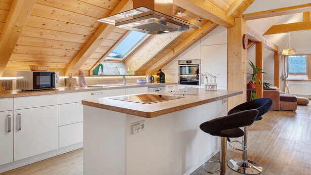 Een moderne keuken met een centraal eiland, houten balken, dakramen en uitzicht op de omgeving.