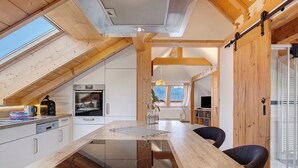 Een moderne keuken met een centraal eiland, houten balken en een schuifdeur in boerderijstijl.