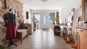 Une pièce avec un mur en pierre, un mannequin, un lit en bois, un bureau et une porte donnant sur l’extérieur.