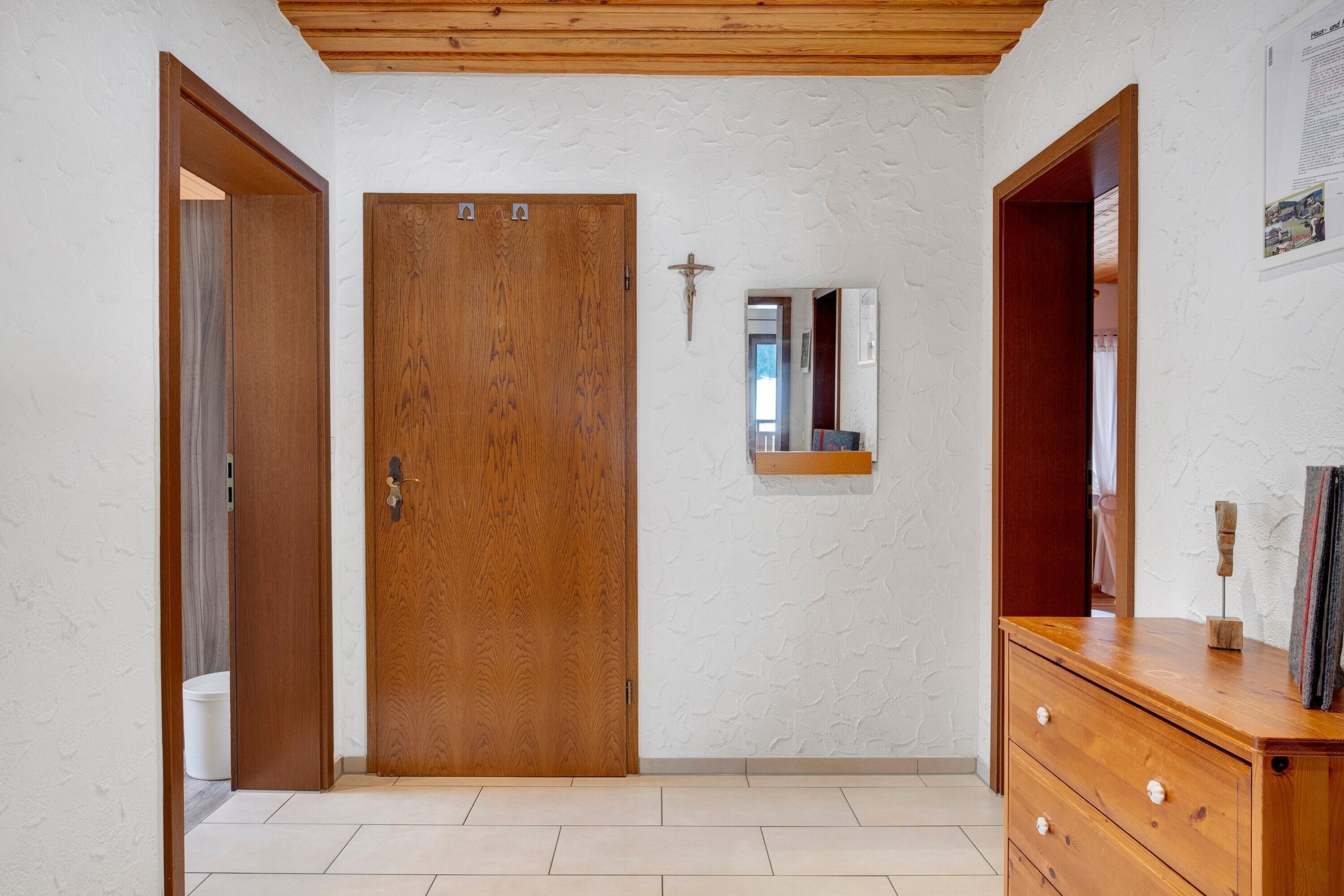 Ein Flur mit Holztür, Spiegel und Holzkommode.