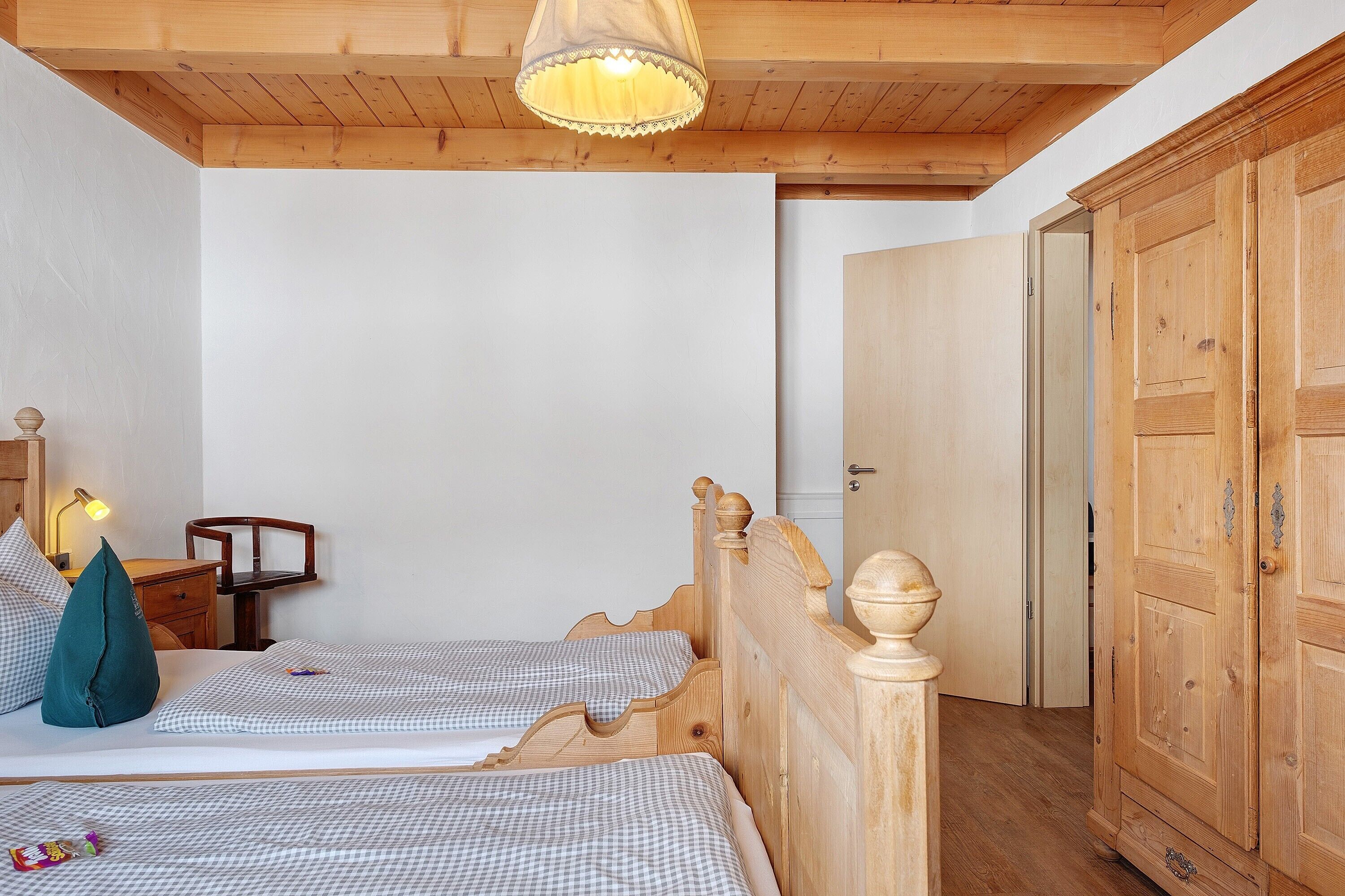Een slaapkamer met twee houten bedden, een nachtkastje, een lamp en een garderobe.