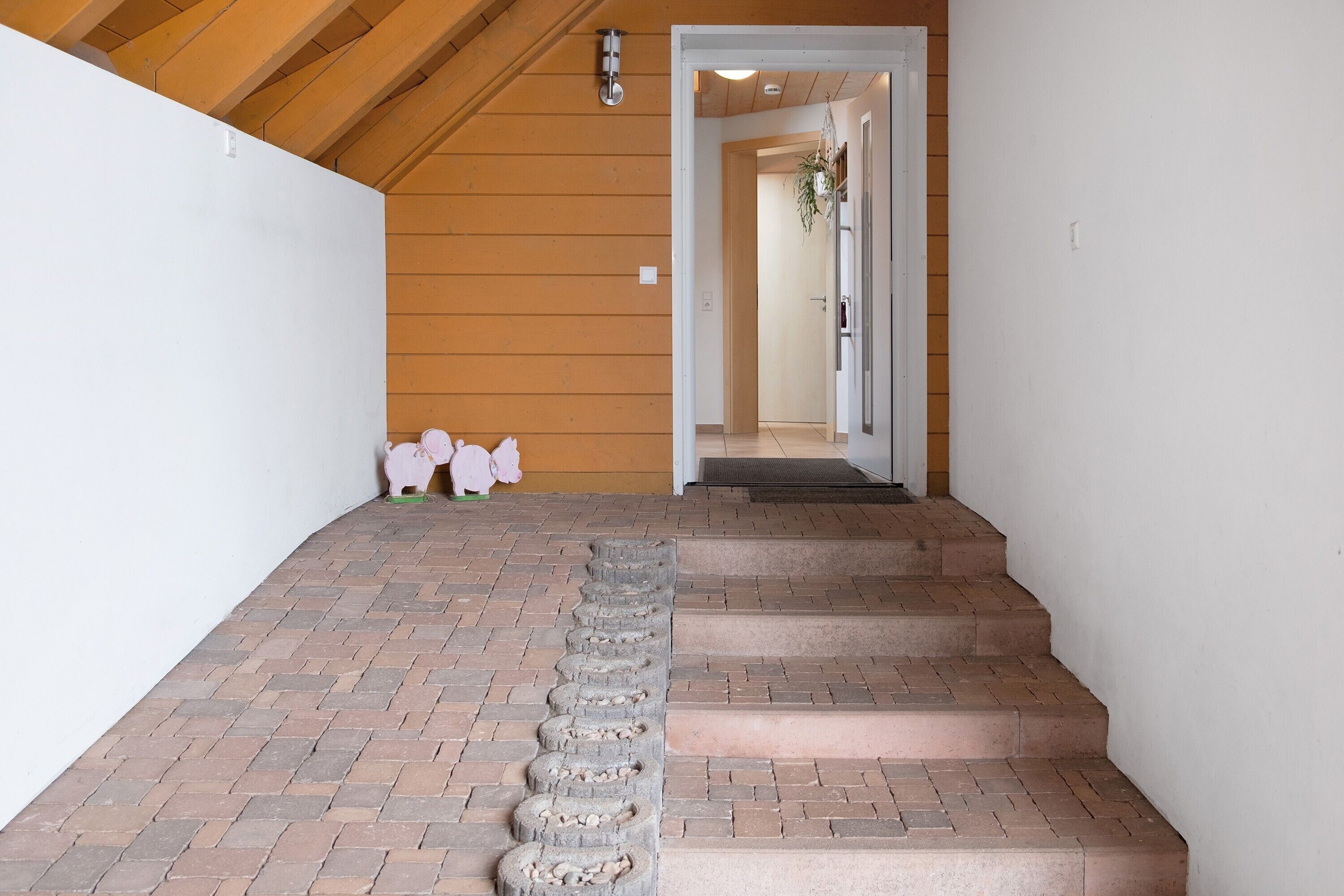 Eine Treppe mit Ziegelstufen führt zu einer Tür, die Wände sind aus Holz und die Decke hat sichtbare Balken.
