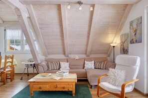 Une pièce confortable de style loft, avec un plafond en bois, un canapé, un fauteuil, une table et des œuvres d’art accrochées aux murs.